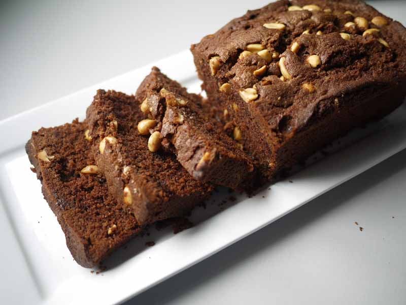 Side view of brown chocolate peanut butter loaf cake studded with peanuts sliced.