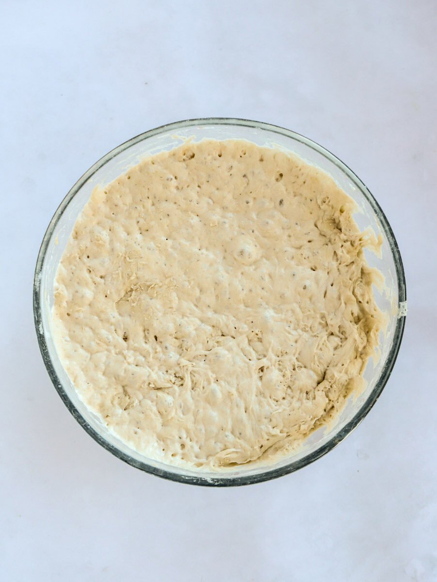 Bread dough mixture in circular glass bowl for for step 2 in the recipe process for No Knead Bread.