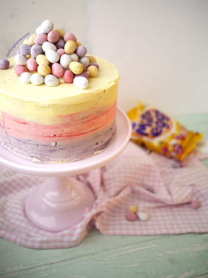 Mini Egg Ombre Pinata Layer Cake on a cake stand with mini eggs in the background.