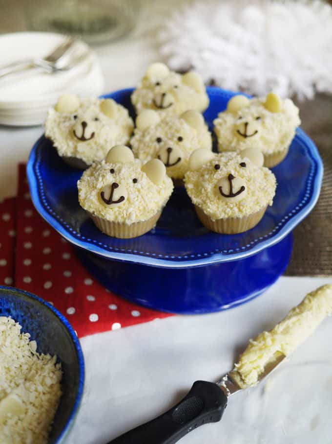 Polar Bear Cupcakes on a blue cake stand, with a festive table in the background.