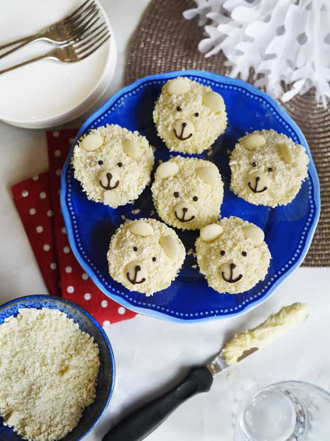 A festive table featuring a blue plate with Polar Bear Cupcakes on, ready to eat.