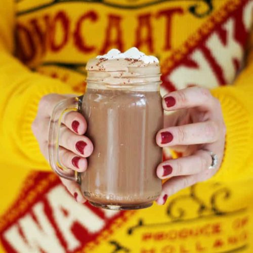 Two hands holding a mug of Advocaat Hot Chocolate with cream on top.