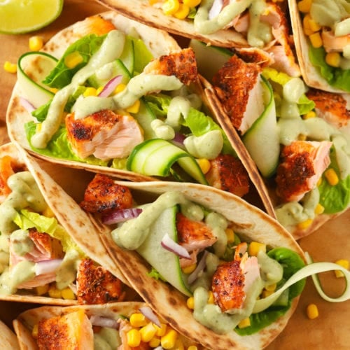 Easy salmon tacos recipe on a wooden board with cucumber and avocado dressing