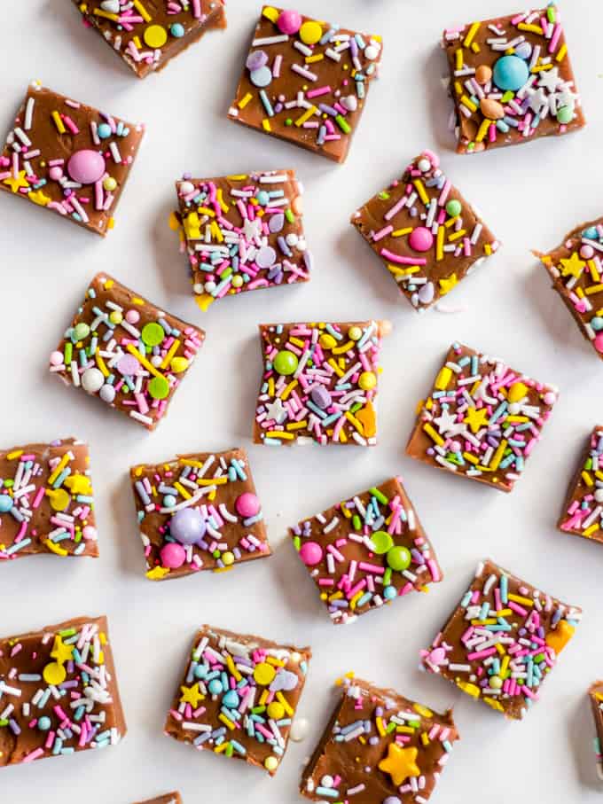 Cubes of chocolate microwave fudge with colourful sprinkles on a white marble background.