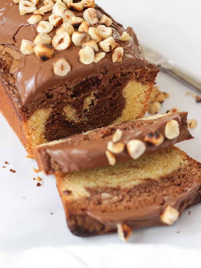Sliced Nutella Cake topped with Nutella and hazelnuts on white background.