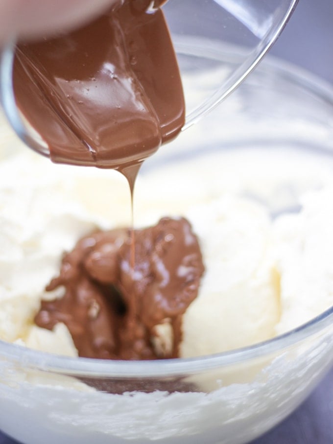 A glass bowl with whipped cream and melted chocolate inside for step 2 in the recipe for Rocky Road Cheesecake.