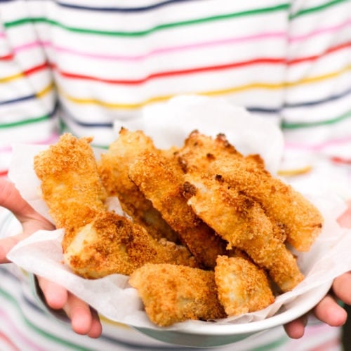 Close up of hands holding a bowl of homemade fish fingers with stripe t-shirt in the background. How to make easy peasy Homemade Fish Fingers using our simple recipe. Just four ingredients and supper tasty family meal every time.