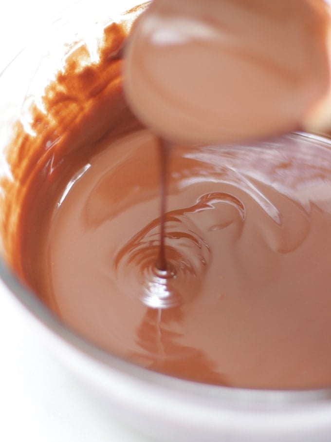 Melted chocolate in a glass bowl with spoon dribbling it into the bowl on white background for Maltesers rocky road recipe.