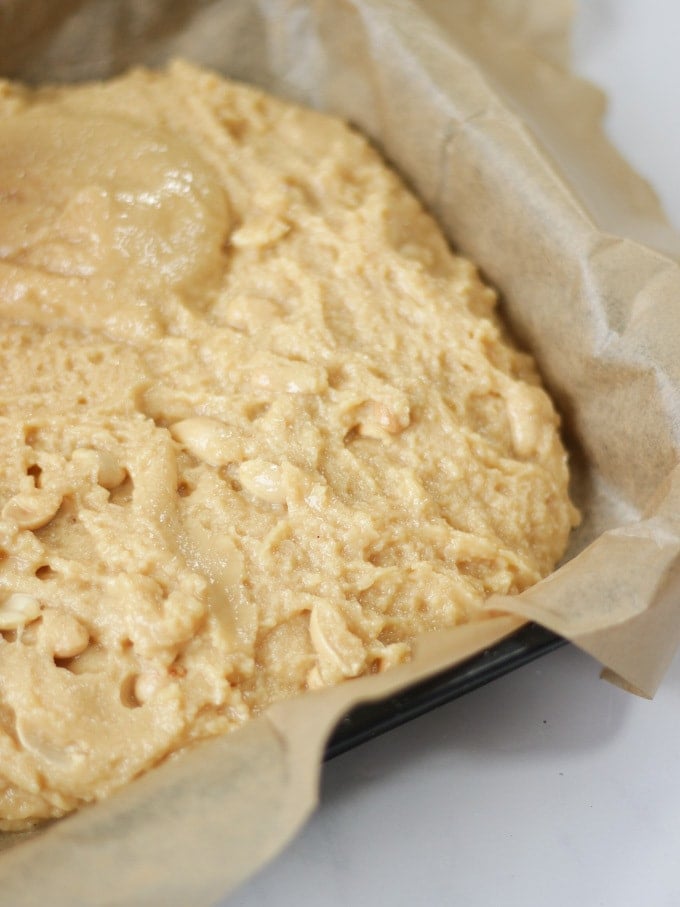 Peanut butter fudge mixture before set in a baking tray lined with baking paper on a white background.