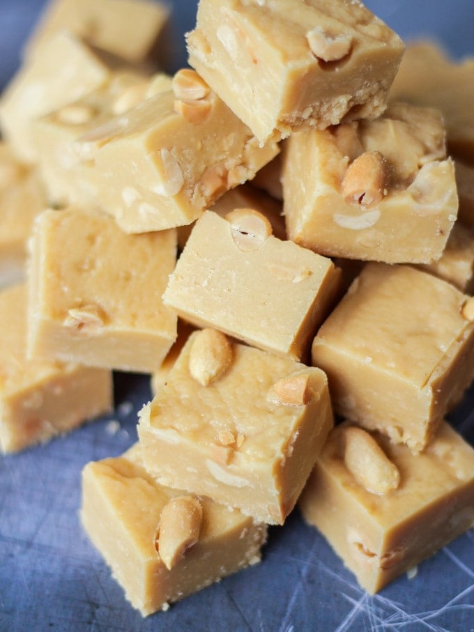 Overhead angled photo of microwave peanut butter fudge cubes with salted peanuts on top on grey background.
