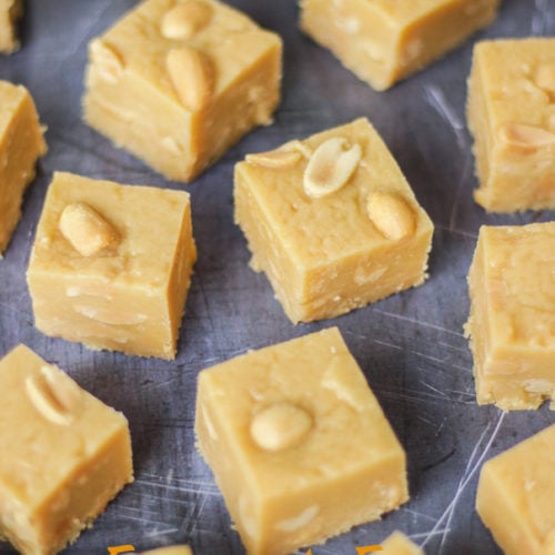 Overhead angled photo of microwave peanut butter fudge cubes with salted peanuts on top on grey background.