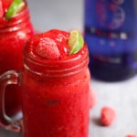 Side photo of raspberry gin frozen cocktails. Adult slushies tipped with raspberries and lime wedges on a grey background.