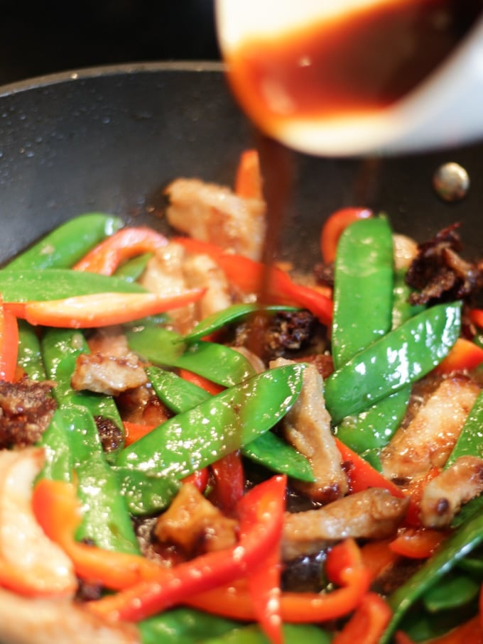 Pork stir fry recipe in wok with sauce being poured in.