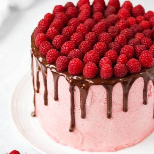Raspberry cake on white plate on white marble background with chocolate ganache and fresh raspberries on top.