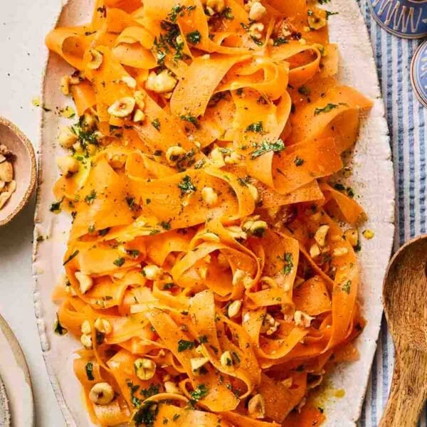 Carrot salad on a long oval platter topped with hazelnuts and dressing.