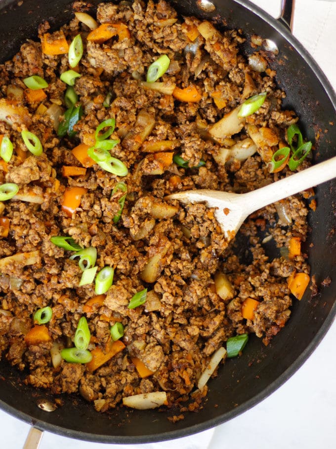 Overhead photo of a black le creuset wok filled with pork yuk sung made with pork mince sprinkled with spring onions with a wooden spoon in the wok.