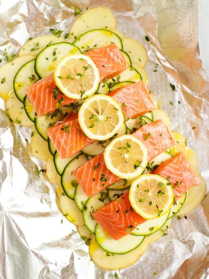Salmon fillets with lemon slices ready to be cooked on potatoes sliced and courgettes.