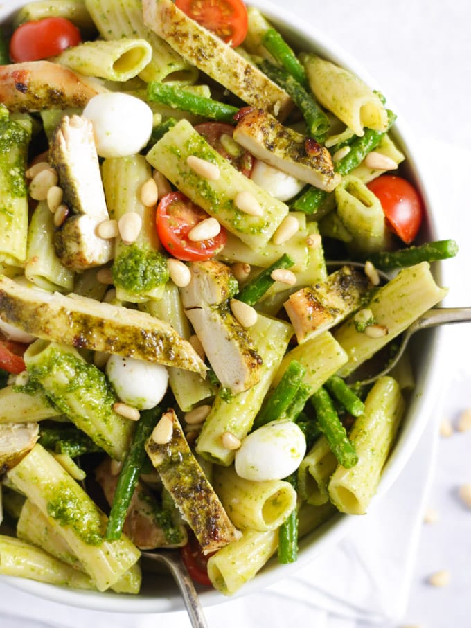 White bowl of Chicken pesto pasta with tomatoes, mozzarella cheese and green beans