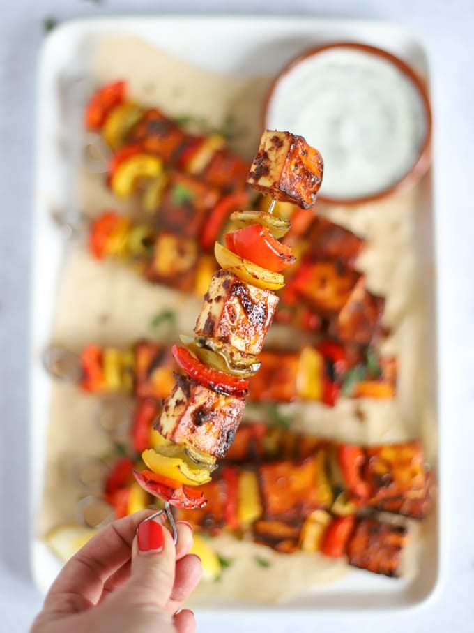 Dry paneer tikka skewers with raita on a tray.
