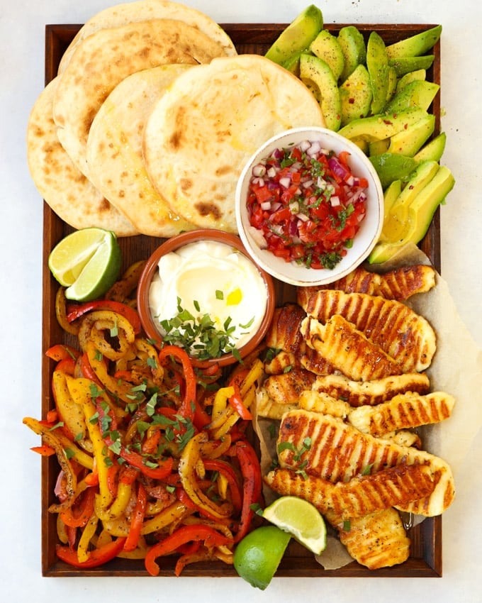 Halloumi fajitas recipe on a board with tortilla wraps avocado and salsa.