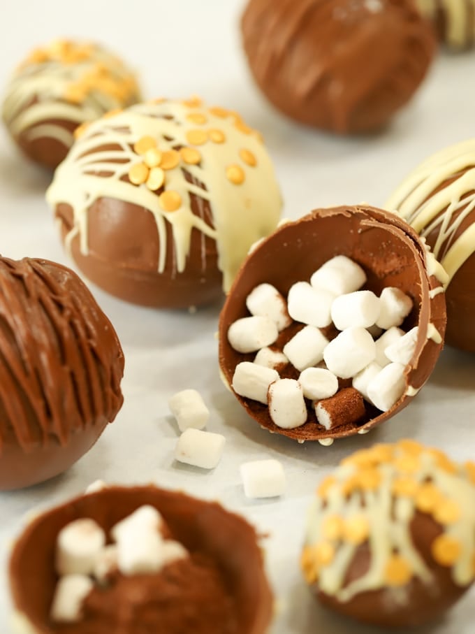 Cocoa hot chocolate bombs on a surface, with one open to reveal the marshmallows inside.