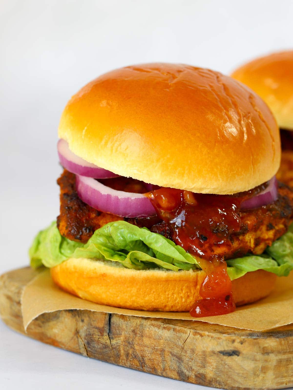 A side angle of a chicken tikka burger, filled with lettuce, red onion and mango chutney.