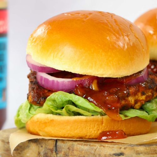 A chicken tikka burger from the side, ready to eat from the wooden board.