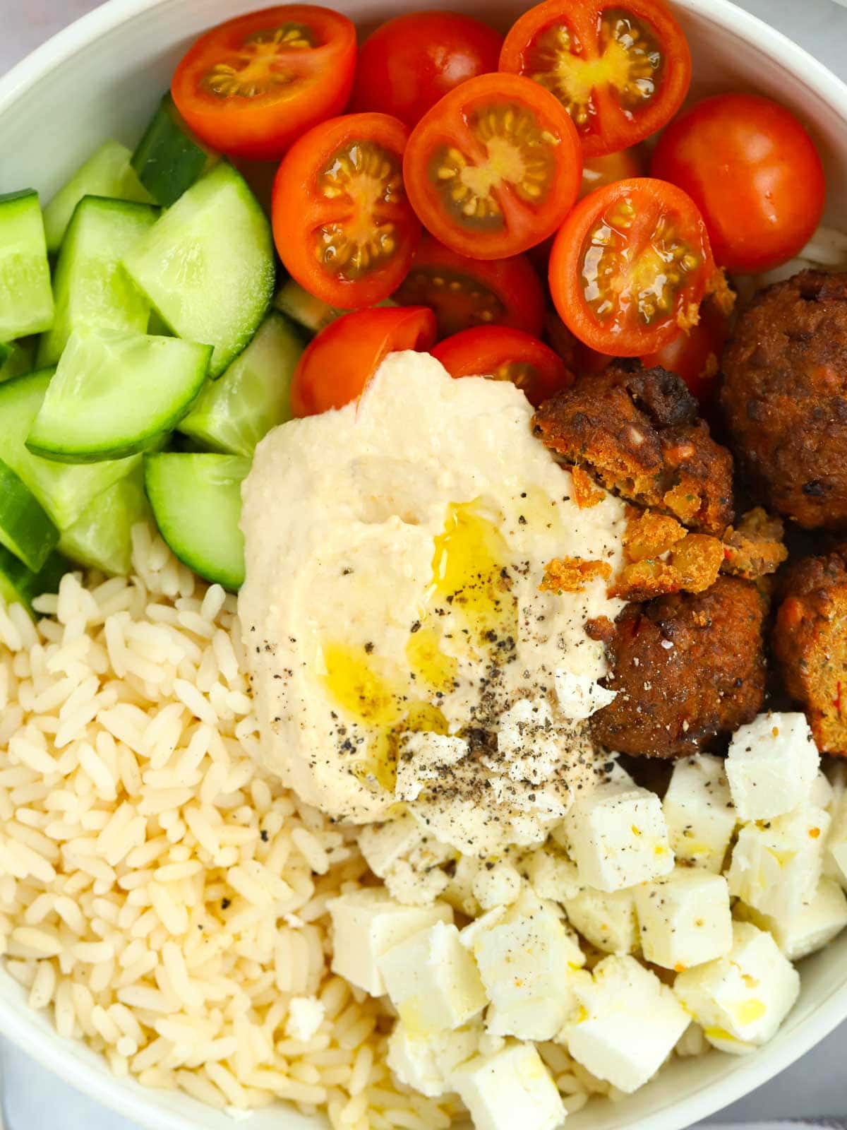 Light Hummus Salad Bowl meal containing rice, hummus, feta cheese, falafel, cucumber and tomato.