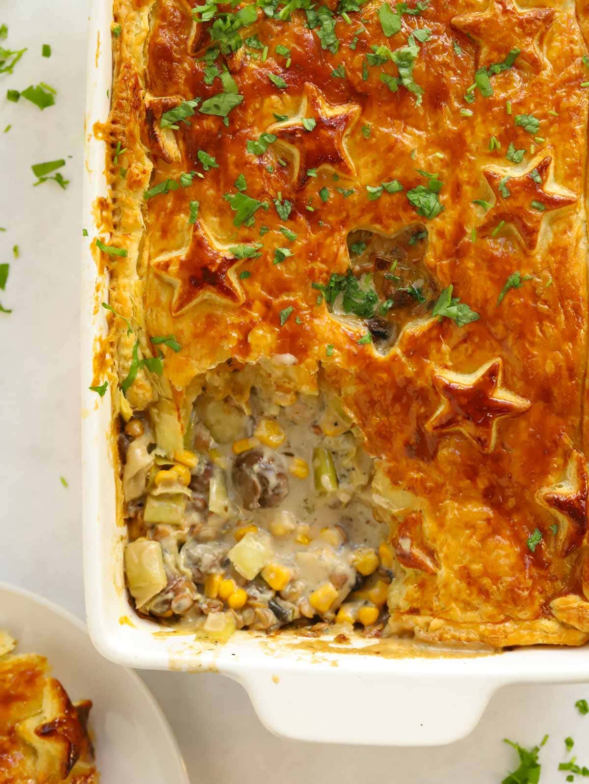 A vegetarian pie with golden pastry crust straight out of the oven with one corner piece missing, revealing the delicious vegetable filling.