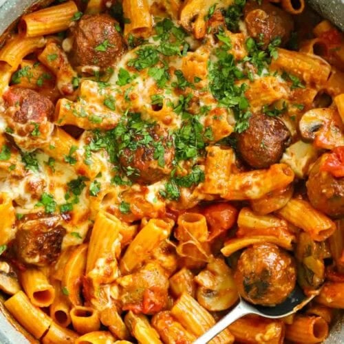 A big one pan filled with meatballs and pasta with tomato sauce and cheese on top.