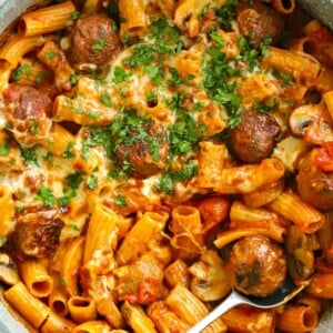 A close up of meatballs mixed with pasta, with melted cheese on top and parsley.