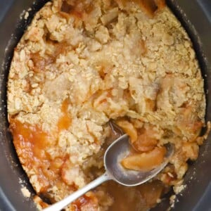 Apple dessert made in a slow cooker, with crumble on top, and a spoon to serve.