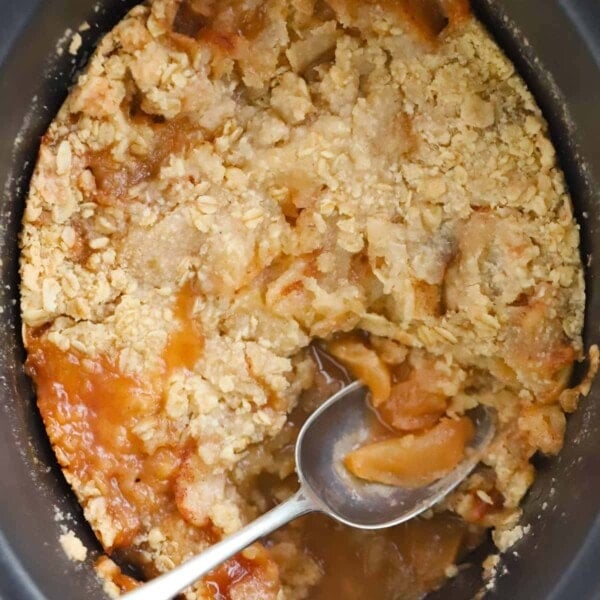 Apple dessert made in a slow cooker, with crumble on top, and a spoon to serve.