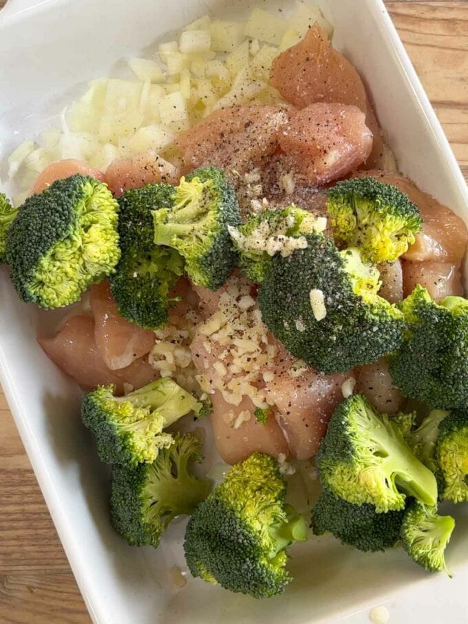 Raw chicken in a dish with onion and broccoli.