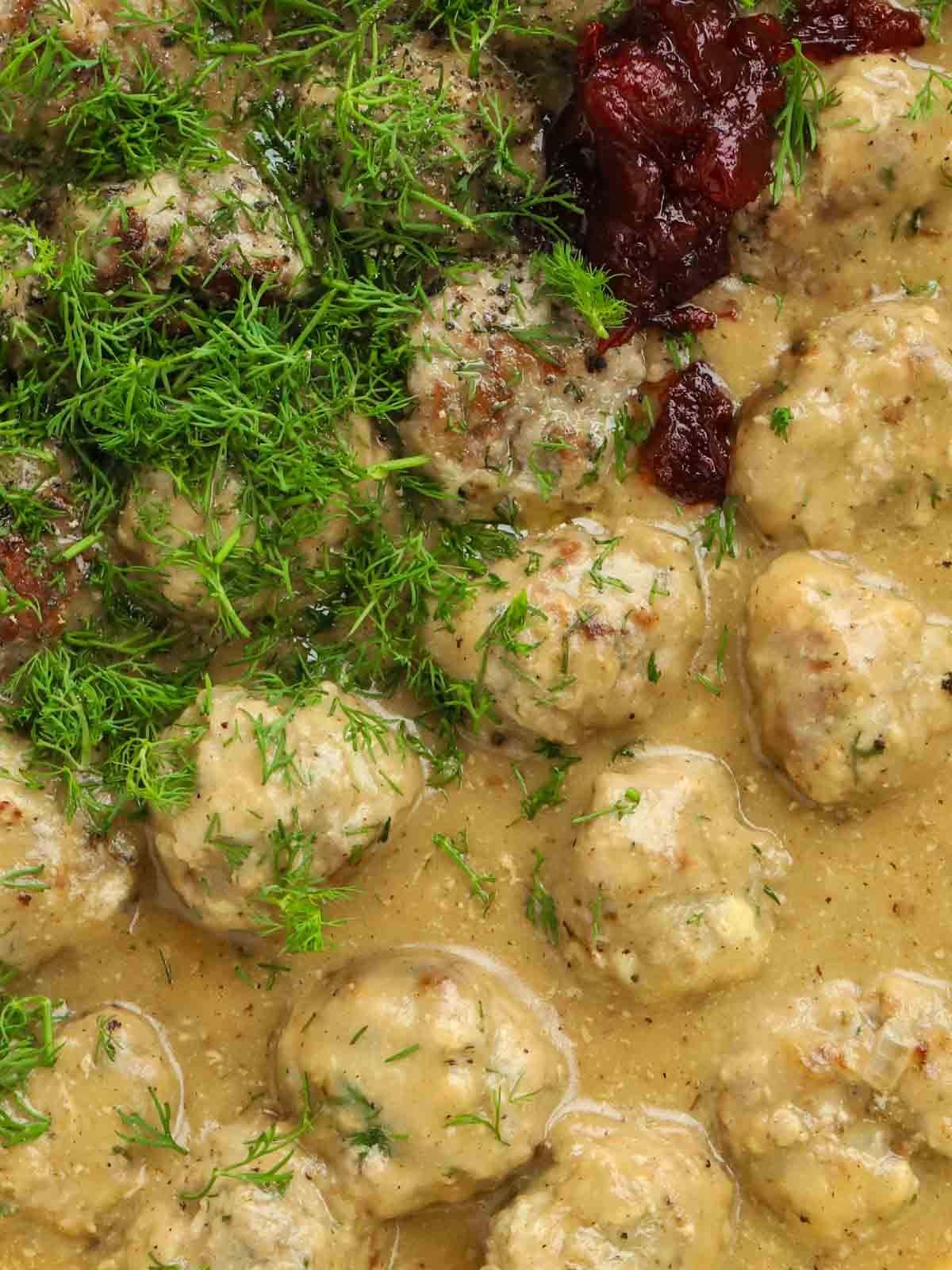 Close up of meatballs in a creamy sauce with fresh dill and redcurrant jelly.