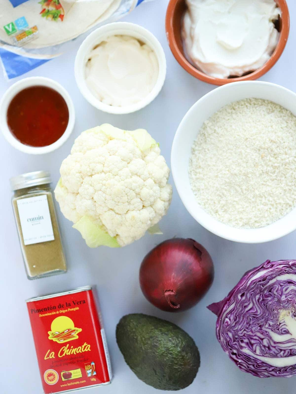 Ingredients including a cauliflower, spices, cheese and tortilla wraps laid out on a counter.