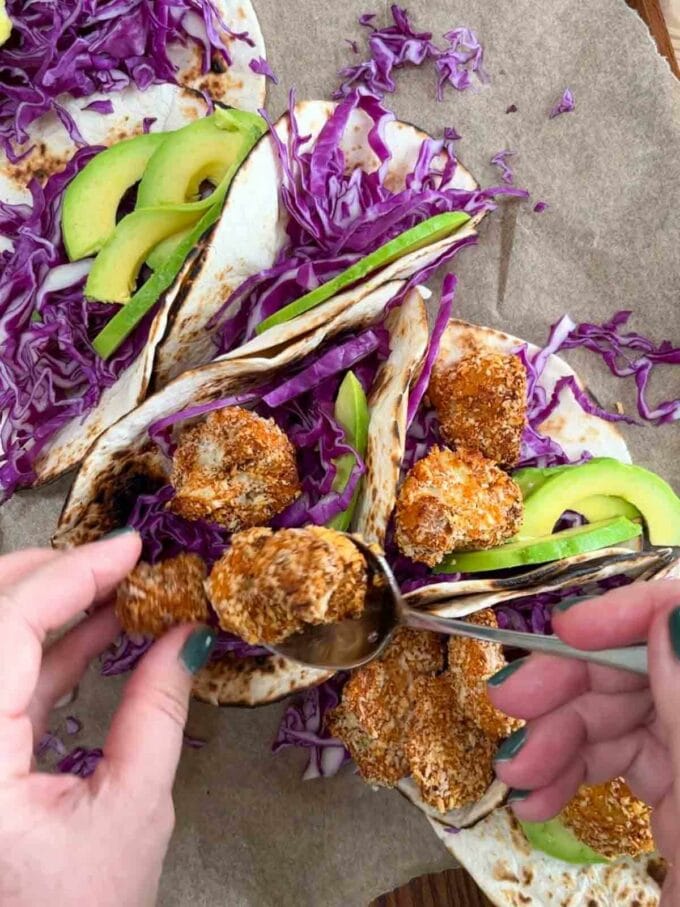 Coated crispy cauliflower being put into a taco with salad filling.