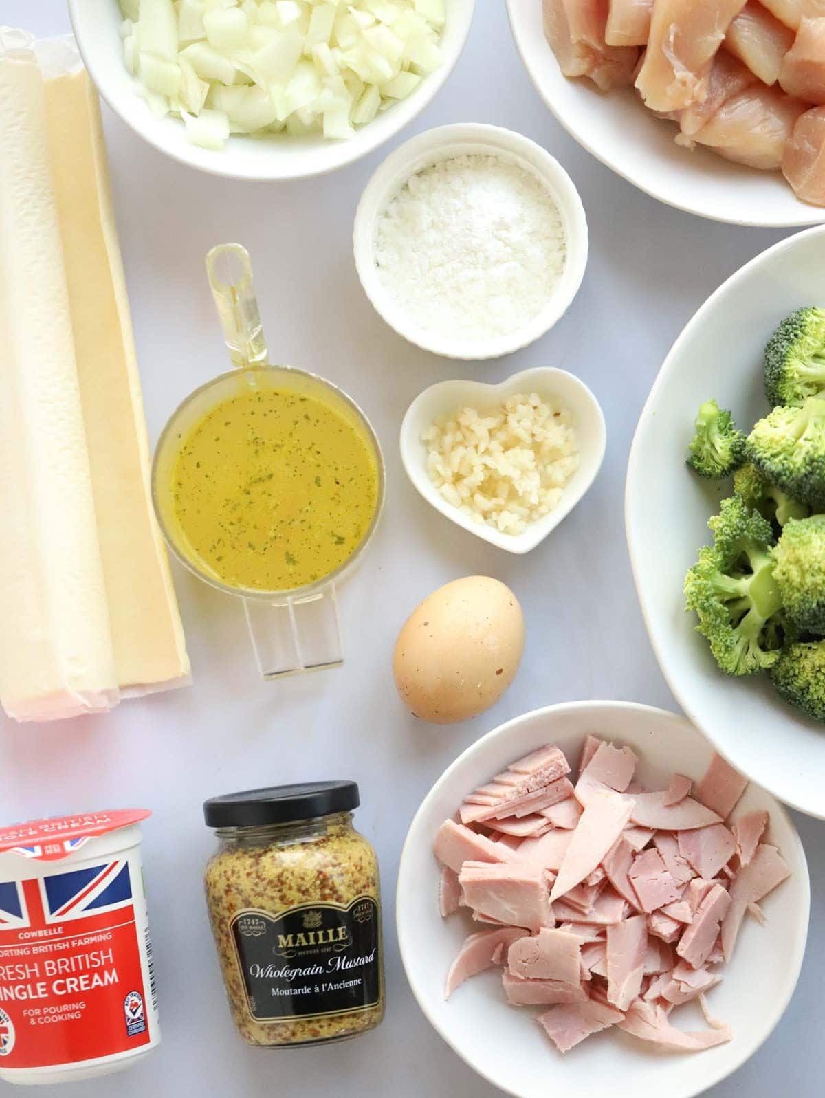 Ingredients laid out on a counter, including raw chicken, onion, broccoli, ham and others.