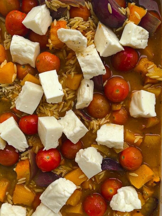 Dried orzo in a dish with tomatoes and cubes of halloumi.