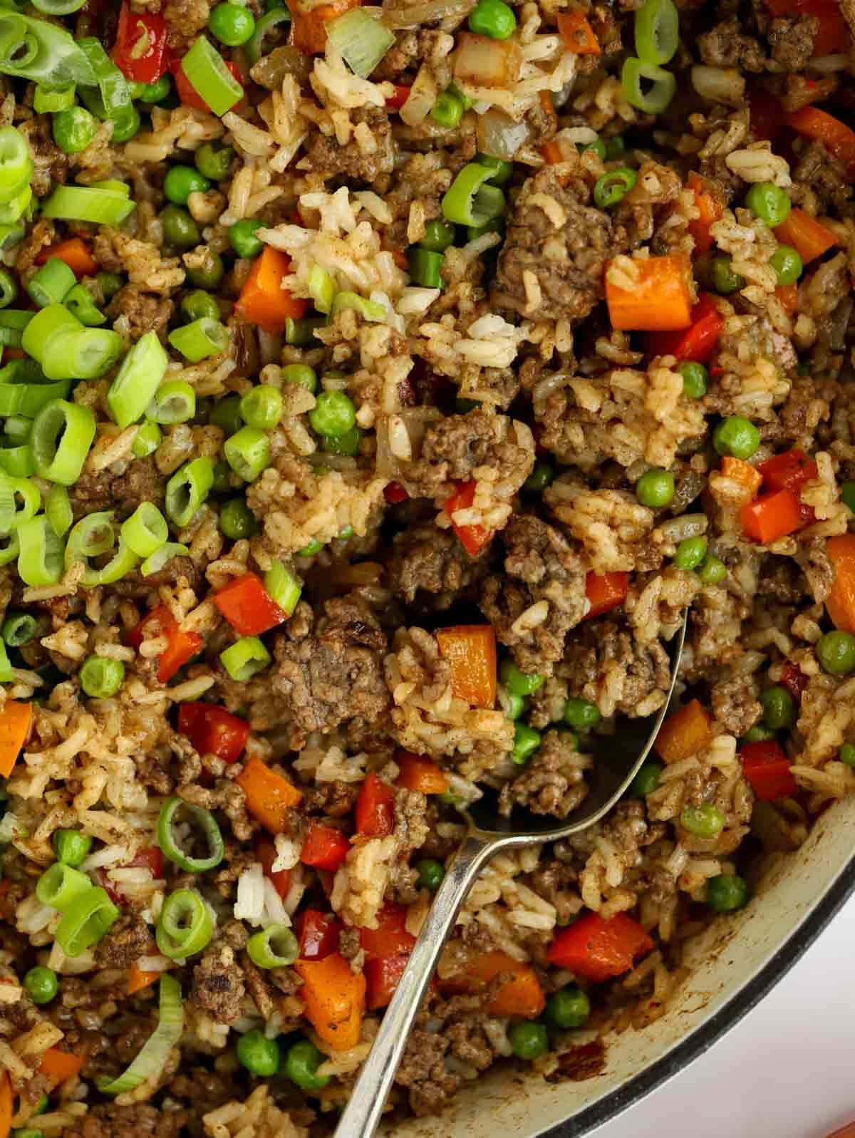 A close up of rice, beef and vegetables mixed together with a spoon ready to serve.