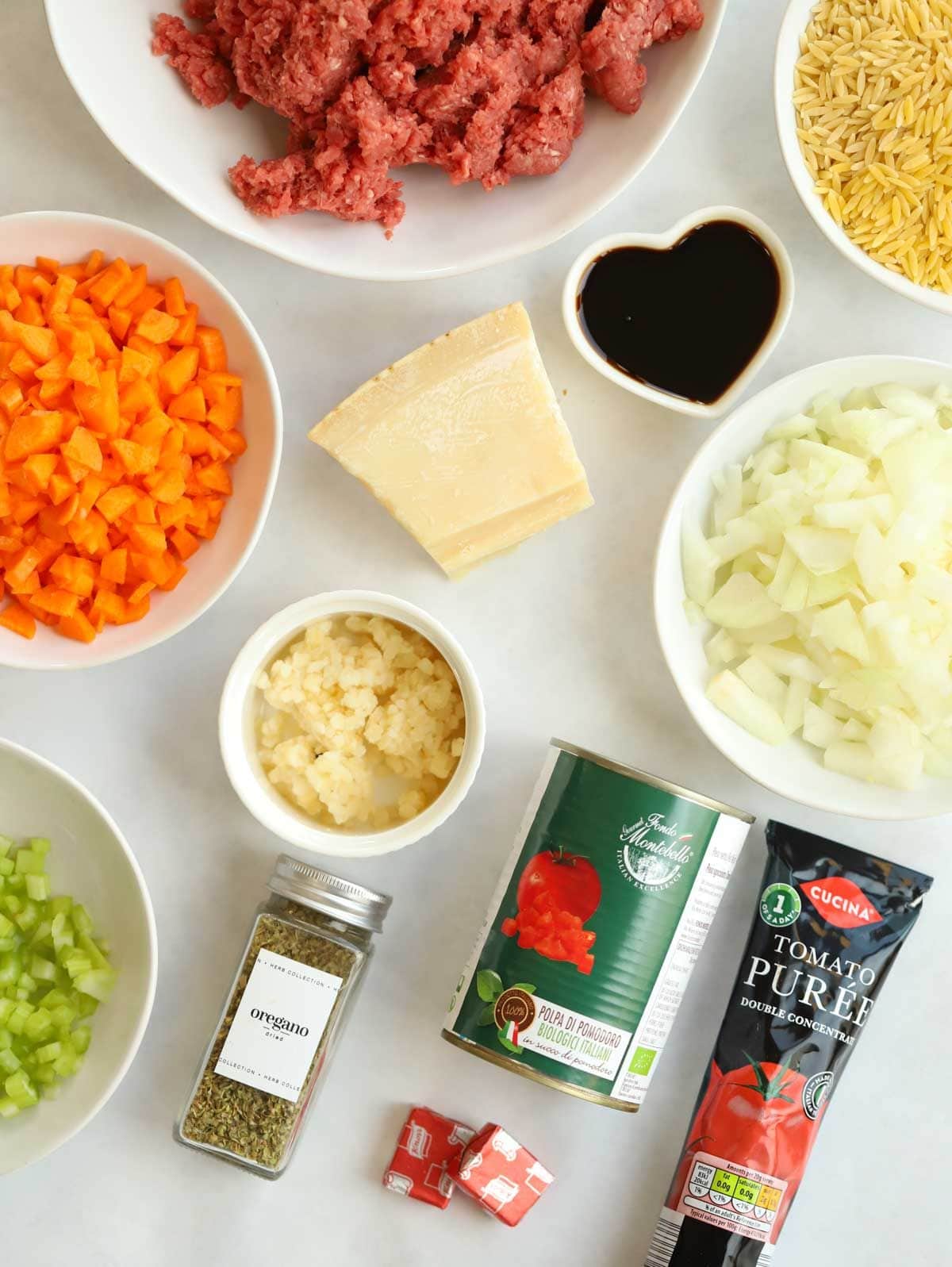 Ingredients laid out on a counter top, including beef mince, tomatoes, onion, carrots, herbs and dried orzo pasta.