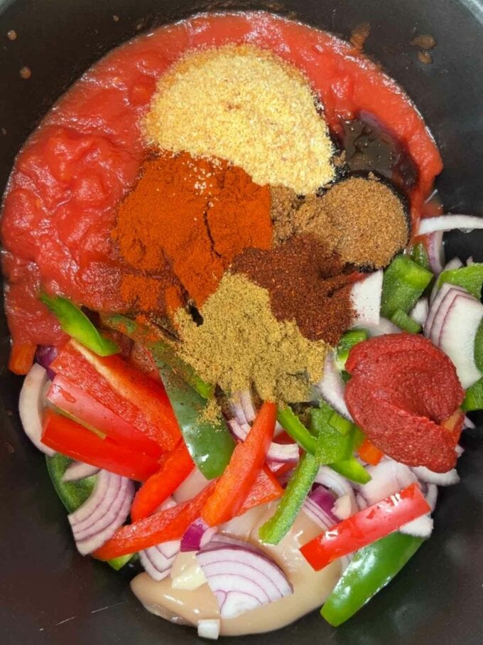 Lots of raw ingredients in a slow cooker, including peppers, tomatoes, spices and chicken.