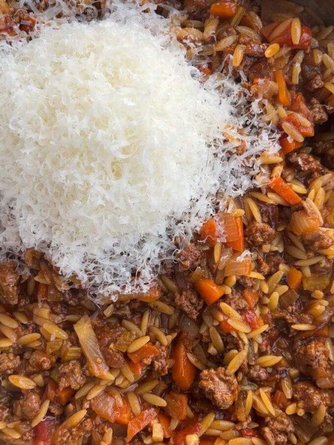 Parmesan on top of a pan of bolognese with orzo pasta.