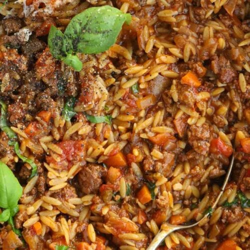 A spoon about to serve up a portion of one pan Orzo Bolognese.