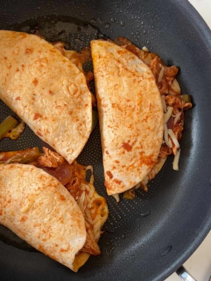 Tacos being fried in a pan.