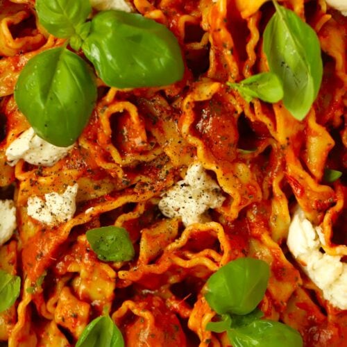 A close up of pasta made with tomato and basil sauce, topped with mozzarella cheese.