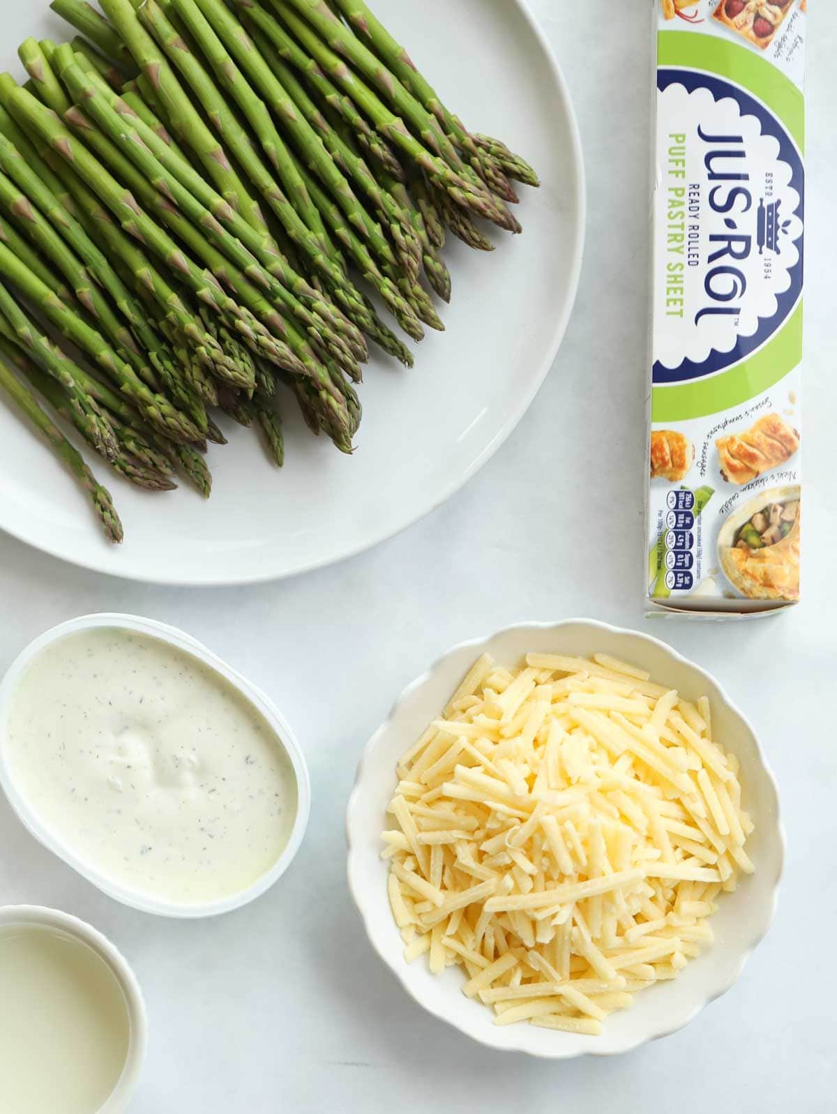 Ingredients including puff pastry, asparagus, cheese and cream cheese laid on a counter.