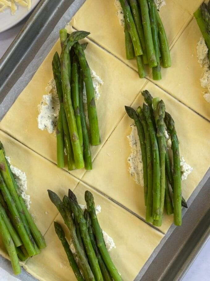 Step 2 in the recipe for Cheese & Asparagus Puff Pastry Parcels. Lay ingredients in pastry squares.