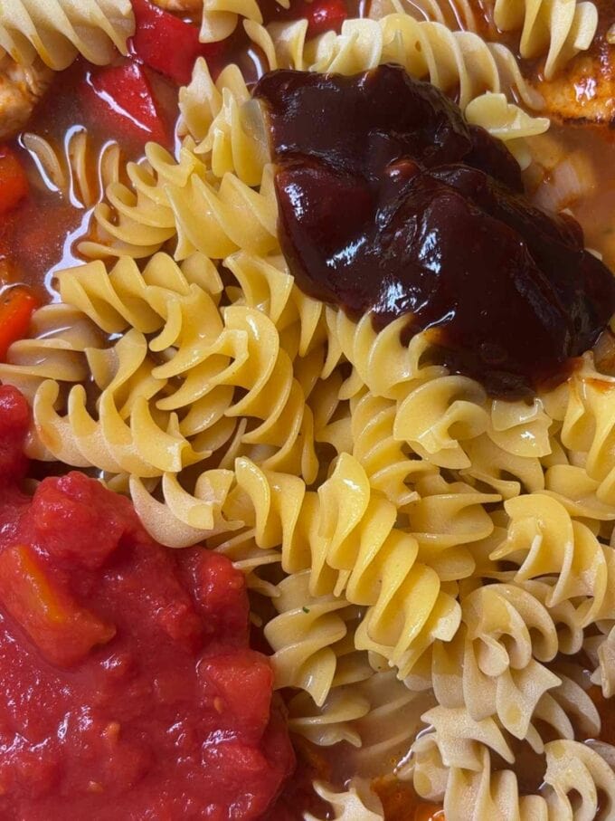 Tomatos, flavouring, pasta and barbecue sauce in a pan.