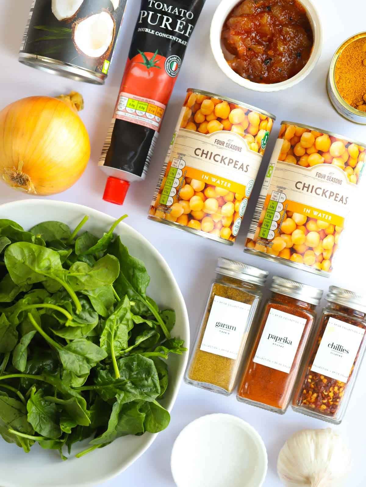 Ingredients including spinach, spices, chickpeas, tomato puree and a lemon laid on a counter.